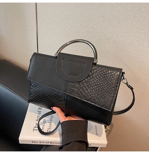 Detail of a black crossbody bag with croc-embossed texture and sleek metal handle