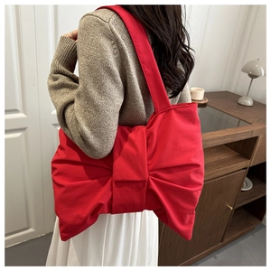 Detail of a red bow-shaped canvas shoulder bag with a soft pleated fabric texture