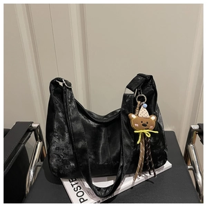 Detail of black metallic leather hobo bag with a cute brown bear charm on a chair
