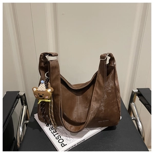 Detail of vintage brown leather tote bag with wide strap and cute bear charm accessory