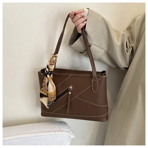 Brown leather tote bag featuring contrast stitching and a decorative silk scarf on the handle