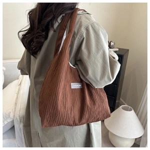 Detail of coffee brown pleated fabric tote bag with white fashion label on shoulder