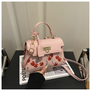Close-up of pink leather handbag with red cherry print and golden metal clasp detail