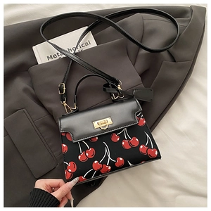 Detail of black PU leather handbag featuring vibrant red cherry prints and gold twist lock