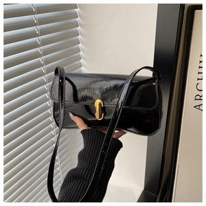 Detail of black patent leather baguette bag featuring a gold rectangular metal lock