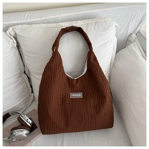 Detail view of large dark brown corduroy shoulder bag with vertical pleats and fashion tag