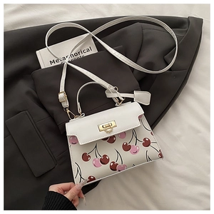 Close-up of white crossbody bag featuring cherry prints and golden metal buckle closure