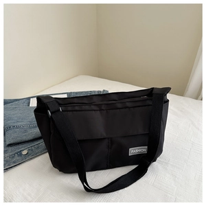Close-up of black canvas crossbody bag with Fashion logo tag and wide fabric strap