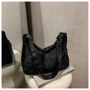 Detail of a black half-moon shoulder bag with matte texture and silver metal buckle