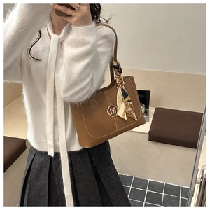 Close-up of brown leather tote bag with metal M logo and elegant floral silk scarf accessory