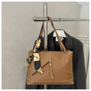Detail of brown leather tote bag showing white contrast stitching and diagonal zipper pocket