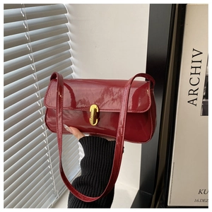 Detail of deep red patent leather shoulder bag with gold rectangular clasp and shiny finish