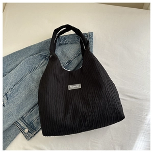 Close-up of black pleated tote bag with FASHION label on light blue denim jacket