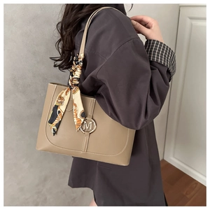 Close-up of khaki leather bag with metal M logo and vintage floral scarf on strap