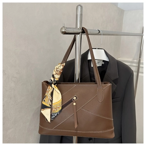 Brown leather tote bag featuring contrast stitching and a floral silk scarf detail on handle