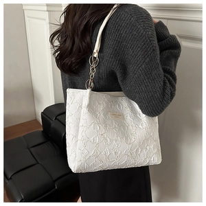 Detail of white tote bag with pleated texture and golden chain strap on shoulder