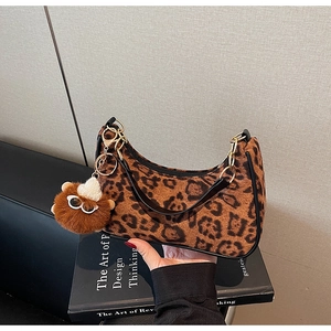 Chic leopard print crescent bag with brown fuzzy charm on decorative design book