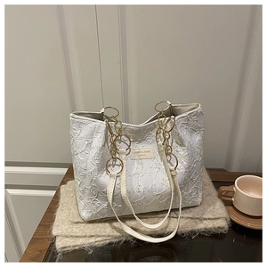 Detail of white quilted tote bag featuring a gold chain strap and chic leather brand tag