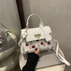 Elegant white crossbody bag with cherry print and gold clasp on a minimalist display