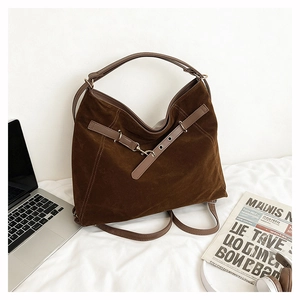 Close-up of brown suede tote bag with metal buckle and straps on white bedding