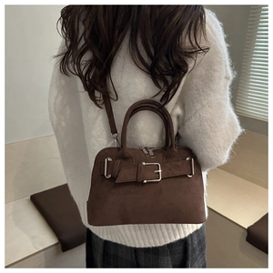 Detail of dark brown suede shell bag with metal buckle on a white knit sweater