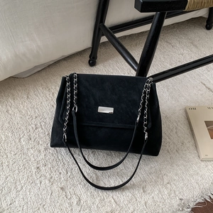 Fashionable black suede tote bag with silver chain strap on a minimalist carpet