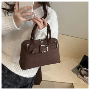 Detail of dark brown suede handbag with metal buckle held by woman in cozy white sweater