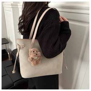 Detail of cream oversized tote bag with side drawstring and plush bear charm accent