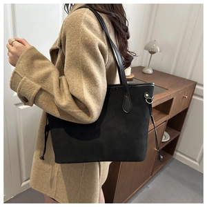 Detail of a large black suede tote bag with a drawstring side on a shoulder strap