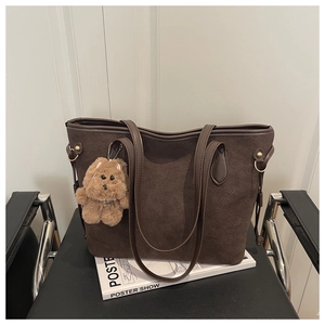 Detail of dark brown matte suede tote bag with plush bear charm on a black chair