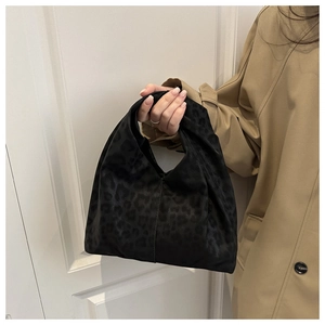 Detail of black leopard print pleated cloud bag held against a camel trench coat