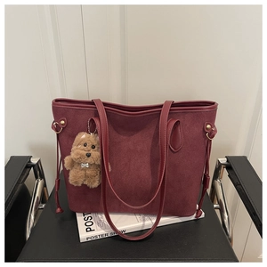Detail of burgundy suede tote bag with drawstring side and plush dog charm on a magazine