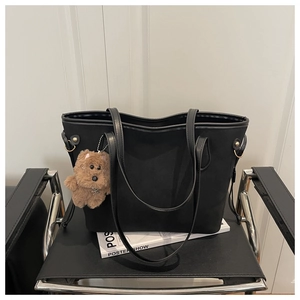 Detail of matte black tote bag with long straps and cute brown puppy plush pendant