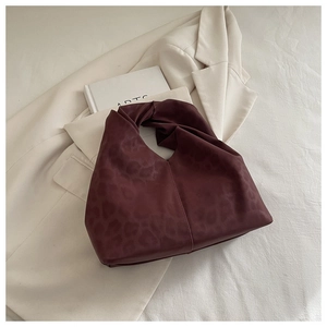 Detail of wine red faux leather handbag featuring leopard embossing and knotted handle