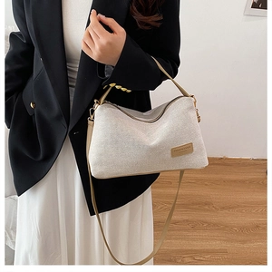 Detail of cream woven handbag with leather logo patch and slim khaki shoulder strap