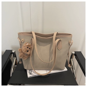 Close-up of khaki tote bag with plush bear pendant on a minimalist chair background