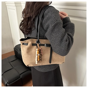 Detail view of large faux suede tote bag with black straps and wooden bead charm