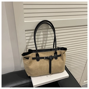 Close-up of khaki suede tote bag with black leather straps on a white decorative surface
