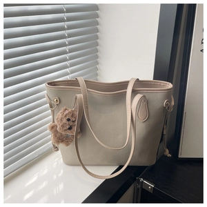 Detail of matte beige tote bag with smooth leather trim and brown plush bear charm