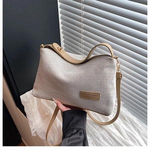 Detail of woven fabric texture and leather logo patch on a chic cream crossbody bag