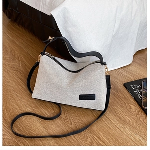 Close-up of beige canvas crossbody bag with black leather trim on a wooden floor