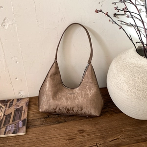 Grand sac à main marron métallisé avec bandoulière posé sur une table en bois rustique