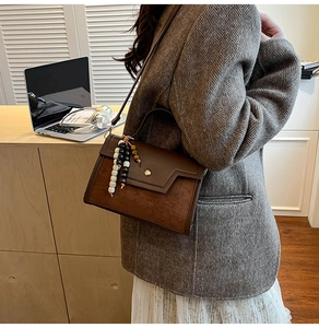 Detail view of leather crossbody bag with beaded pendant in a casual office setting