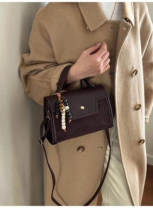Detail of vintage brown leather bag with boho beaded tassel on beige wool coat