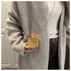Close-up of a mini gold metallic crossbody bag with chain strap on a knit cardigan