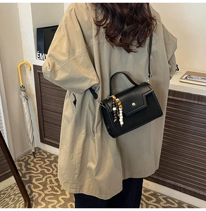 Structured black leather handbag with gold buckle and beaded charm shown on model