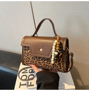 Detailed view of leopard print leather handbag with wood bead tassel and gold buckle