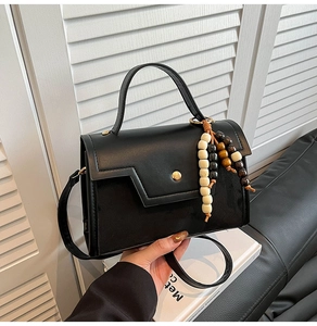 Close-up of black matte faux leather handbag featuring a golden clasp and beaded pendant
