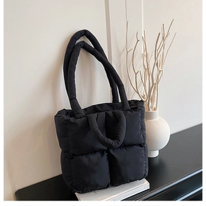 Detail of black quilted puffer tote bag with padded handles on a minimalist studio set