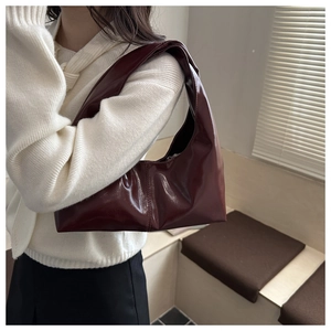 Detail of burgundy hobo bag with glossy finish and stylish knotted handle on shoulder